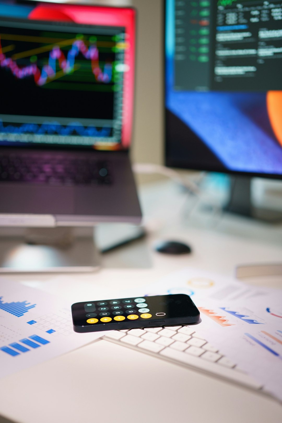 Smartphone on financial documents near laptop with stock charts.